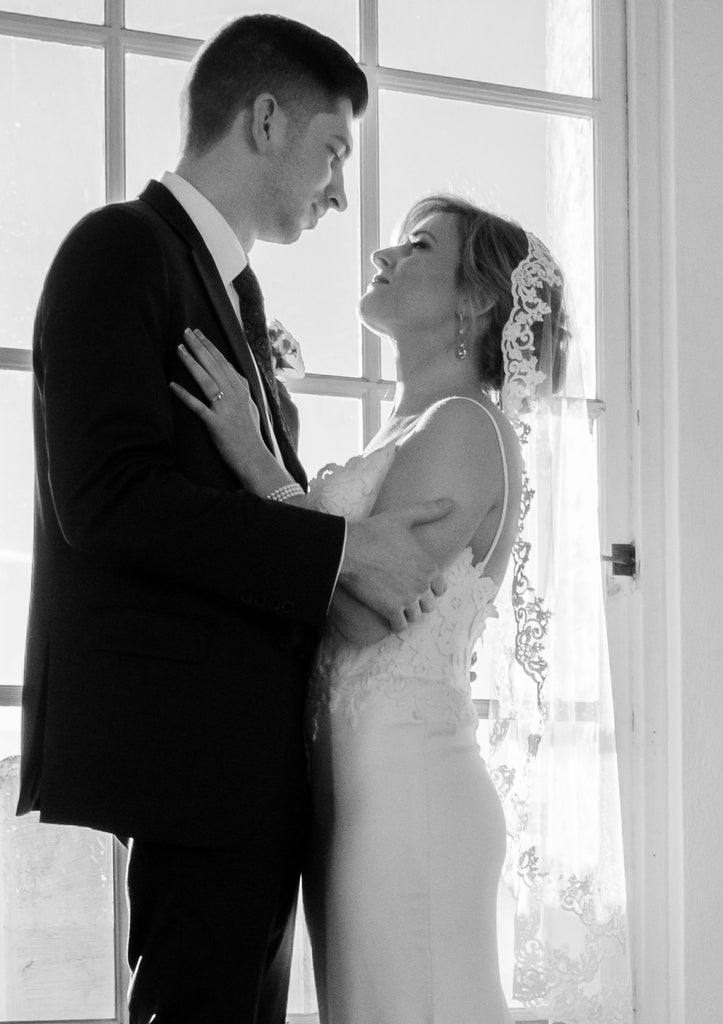 romantic lace bridal veil mantilla on top of bride's updo as she looks at groom