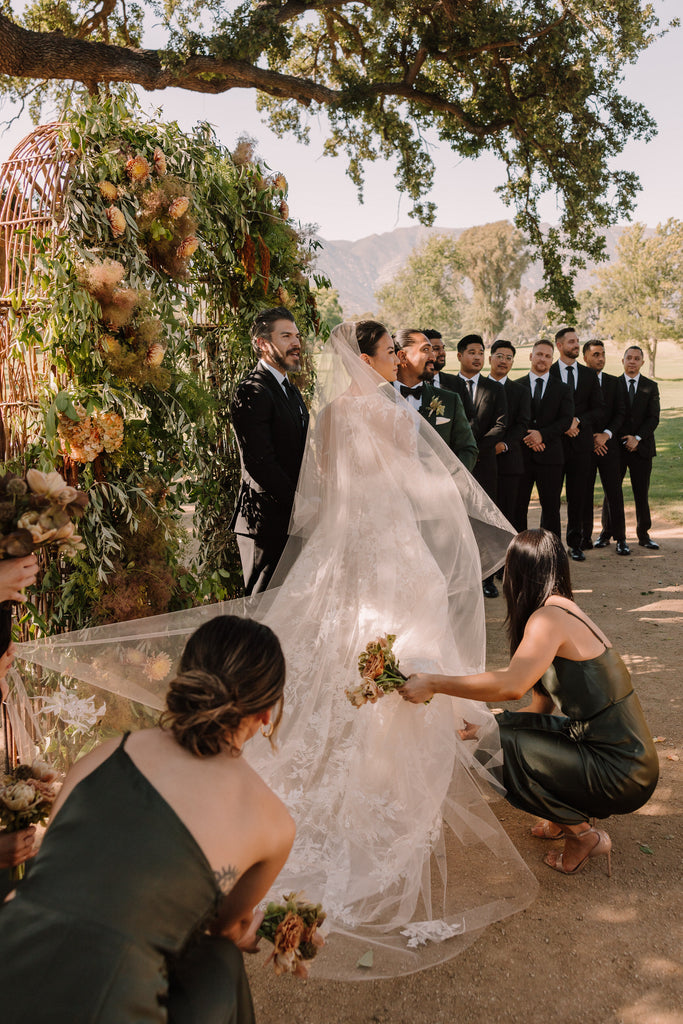 bridesmaids in green gown fixing two layer cathedral bridal veil with lace applique for outdoor romantic