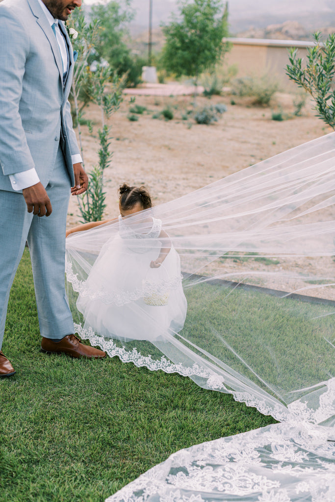 flower girl helping with lace cathedral length wedding veil on lawn for bride