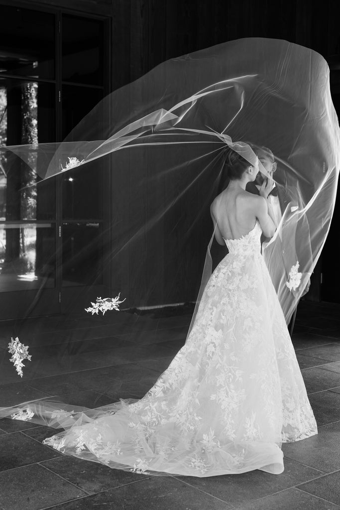 elegant long appliquéd lace wedding veil in wind as couple embraces