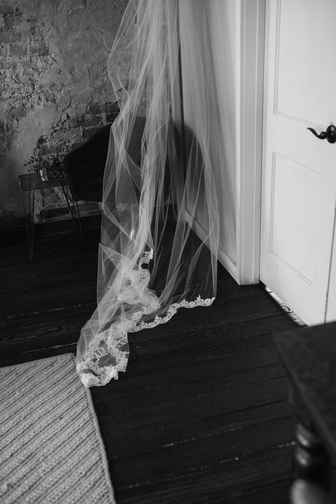 French lace trimmed long cathedral wedding veil hanging on door