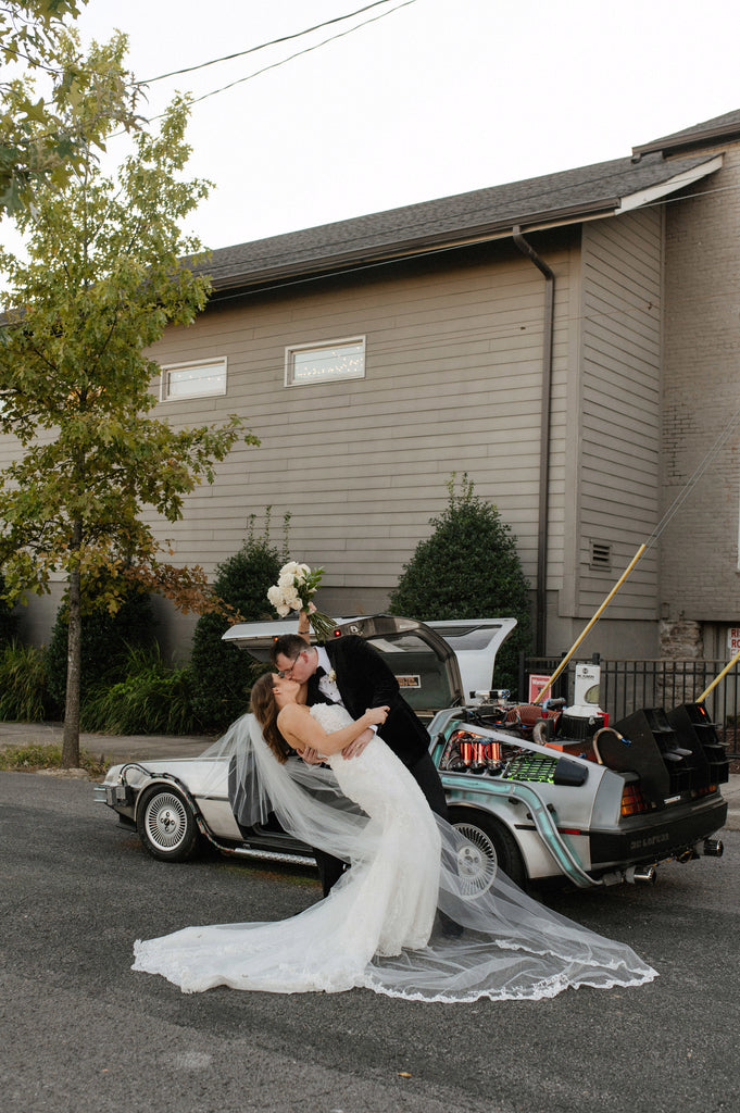 lace cathedral bridal veil with lace and custom embroidery as bride and groom kiss in front of futuristic car
