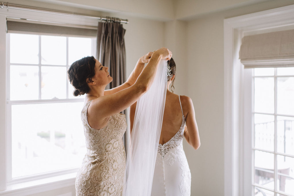 bridesmaid in champagne dress putting long bridal veil in ivory into bride's updo