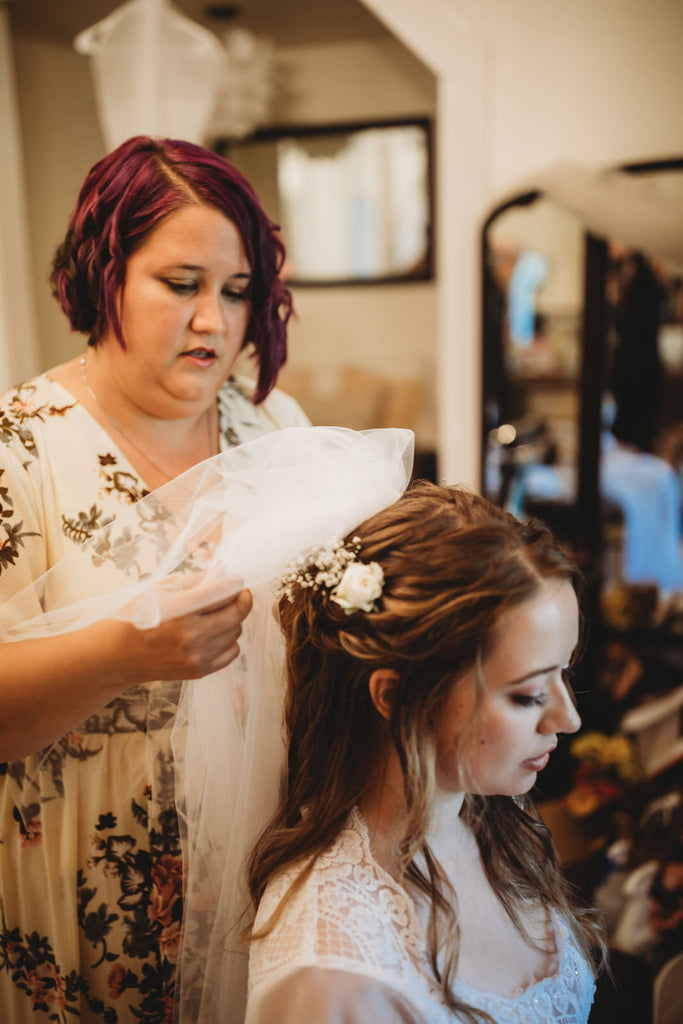 bridesmaid putting wedding veil in bride's half up hairstyle with flower hair pin