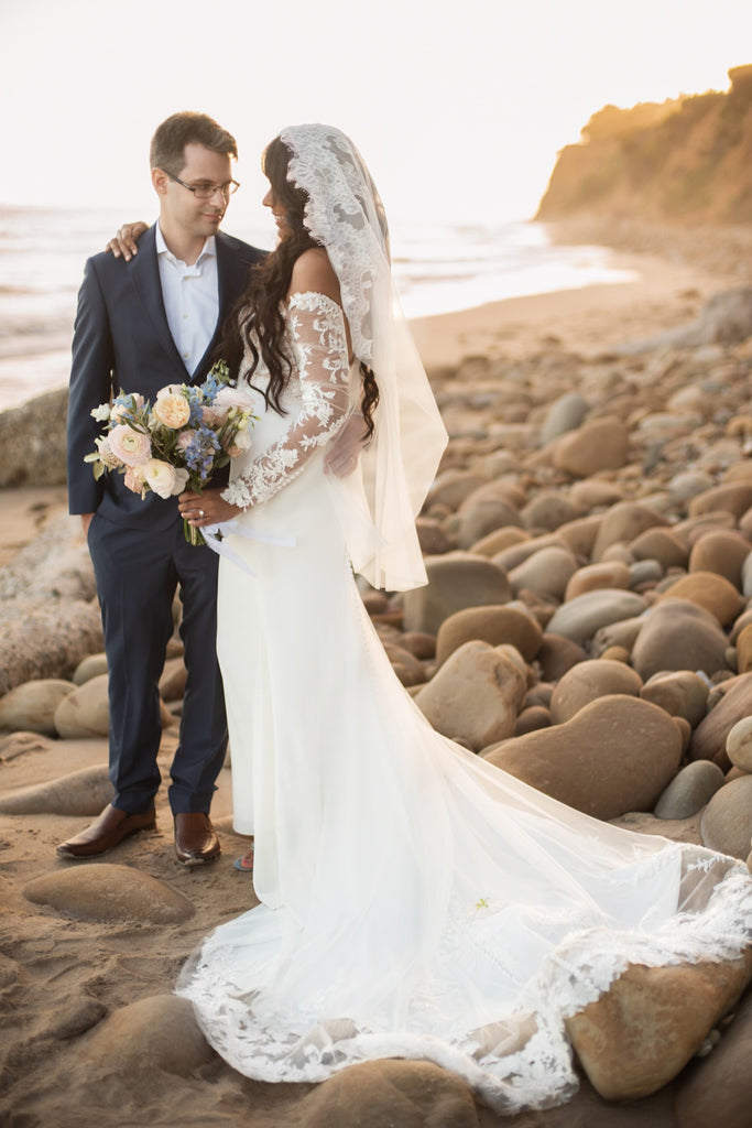 beach sunset wedding with bride in fingertip lace mantilla wedding veil on top of head in traditional spanish style