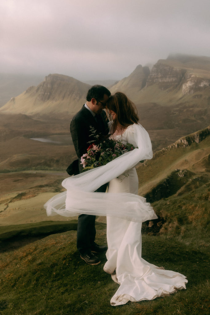 romantic Scottish destination wedding with long sleeve gown and bridal wings blowing in wind