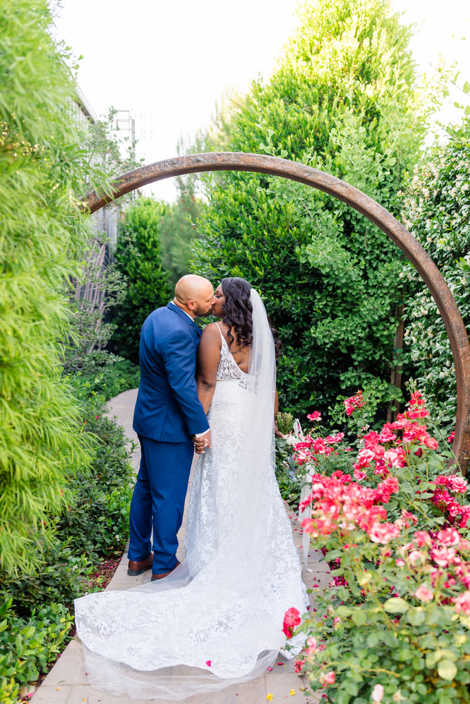 garden wedding with couple under archway and long scattered pearl cathedral length bridal veil in curled hair downdo