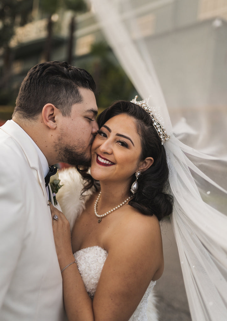 black tie formal wedding with bride in gold tiara and silk cathedral wedding veil as groom kisses her cheek