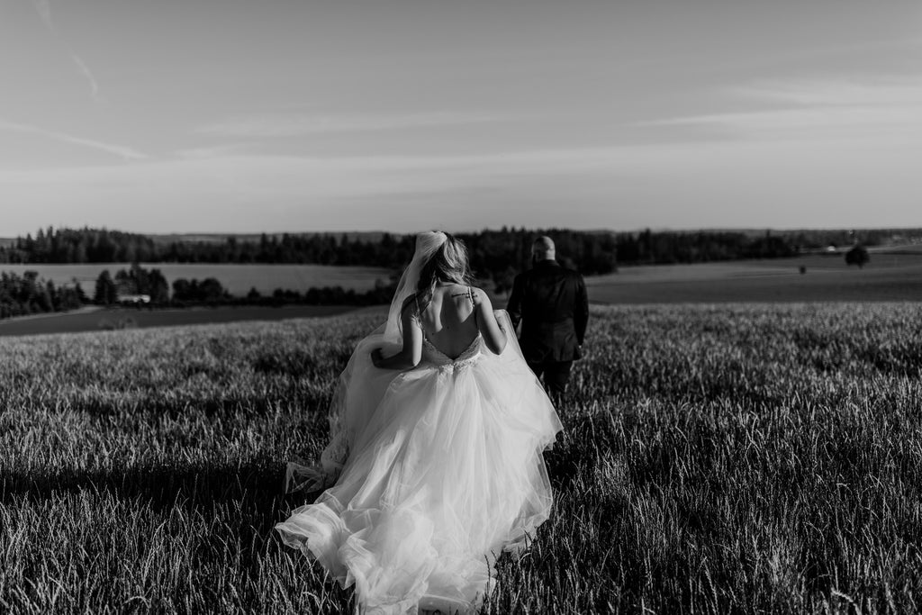 bride in fluffy tulle chiffon ballgown walking through meadow with long royal length veil to reach her groom