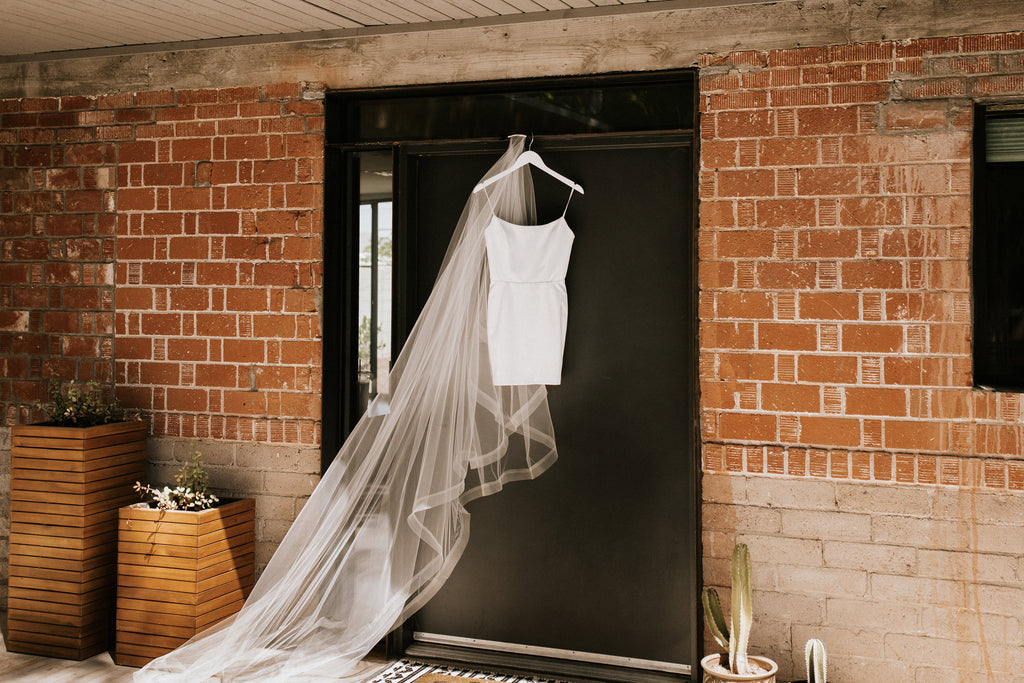 short wedding dress with long horsehair ribbon drop cathedral length wedding veil hanging on door