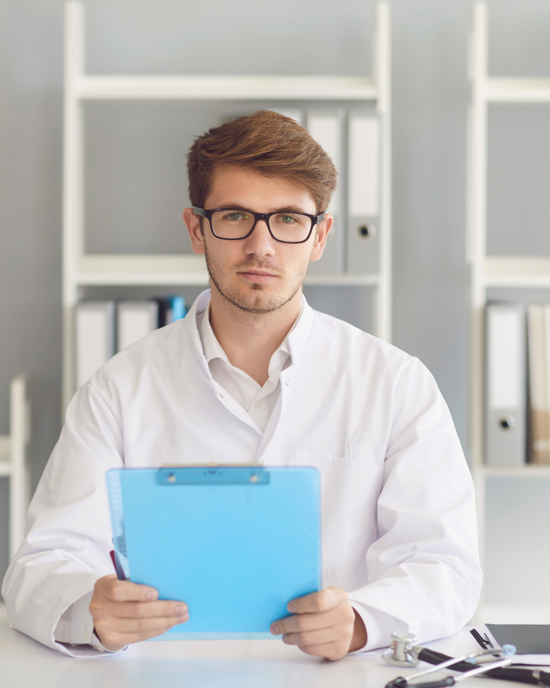 Male nursing student wearing white lab coat and holding clipboard