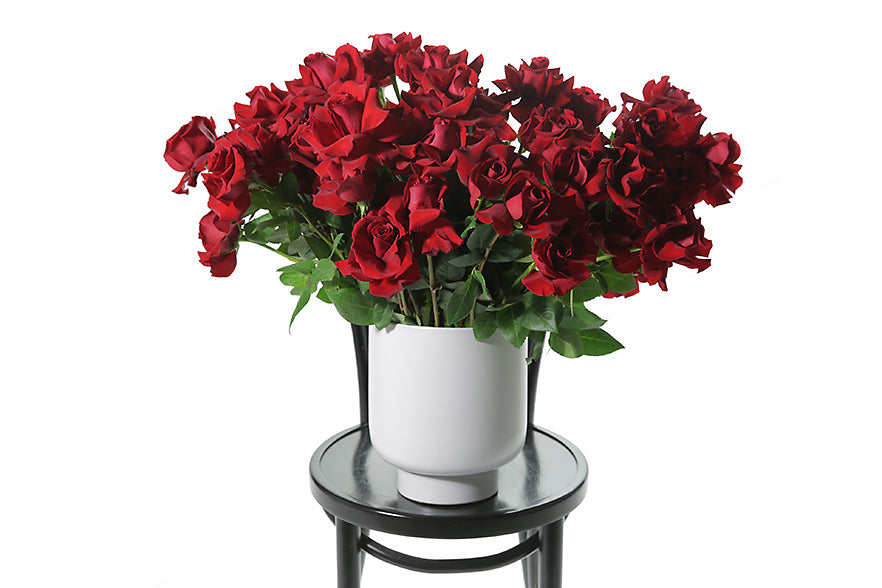 Red roses in a white vase displayed on a black chair
