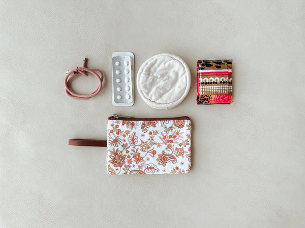 A compact bag stocked with medicine, pads, and other personal care items for a woman.
