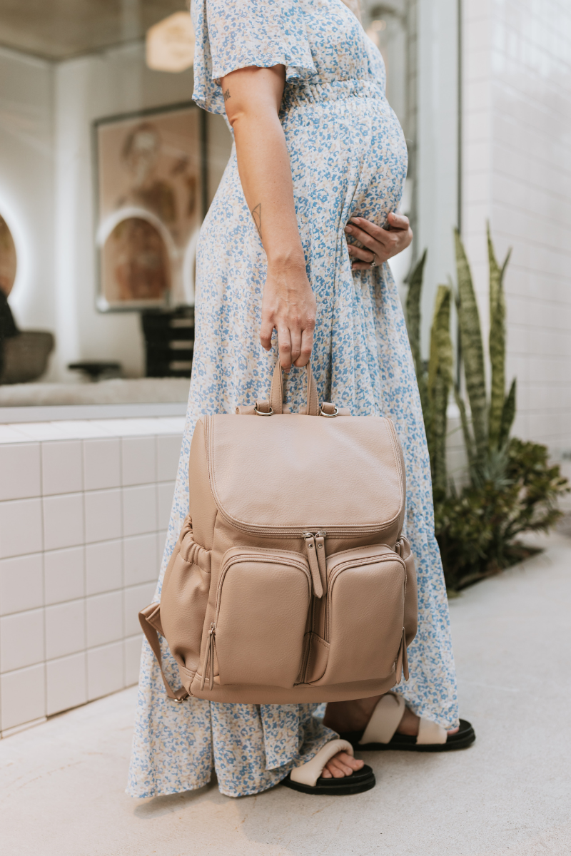 pregnant mum to be wears blue maternity gown with oat nappy backpack