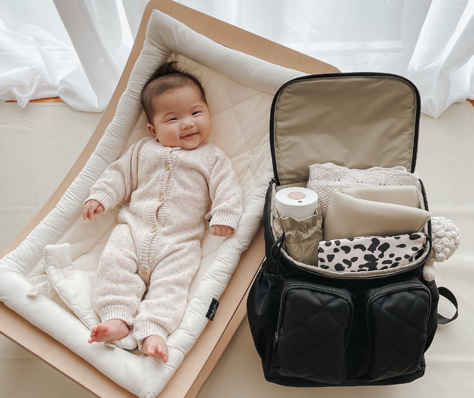 Baby sitting in a rocker with a packed nappy bag nearby, ready for an outing