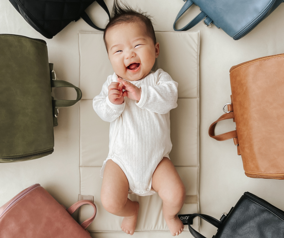Baby surrounded by various types of baby bags: diaper bag, nappy backpack, and tote