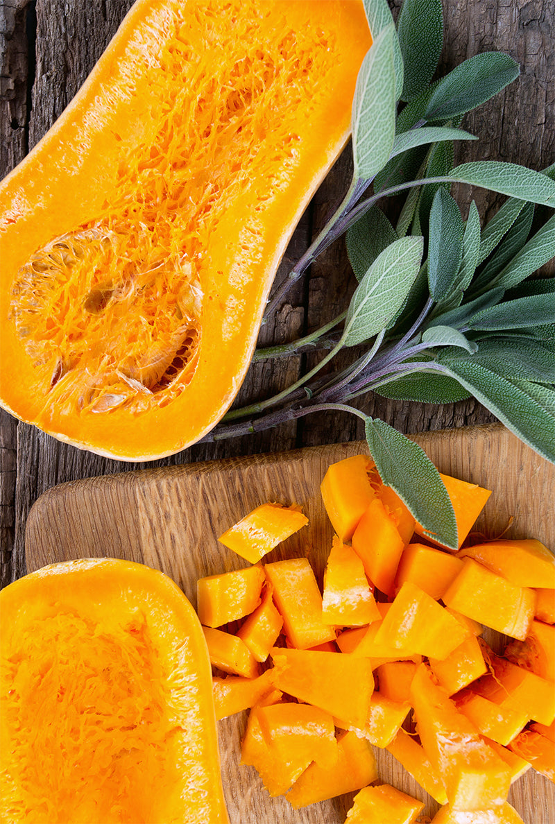 Cross-section of butternut squash with sprigs of sage and cubed squash pieces