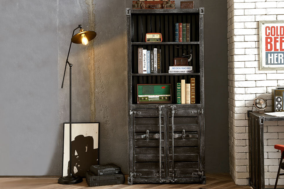 Vintage style industrial shelf with half doors stocked with books and decor. Set in a room with concrete walls and exposed white washed brick.