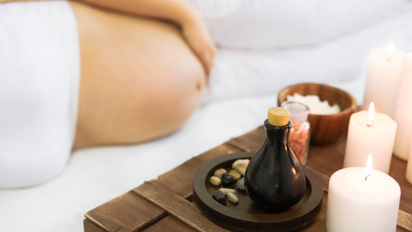 Pregnant woman lying on a massage table next to massage oil and candles