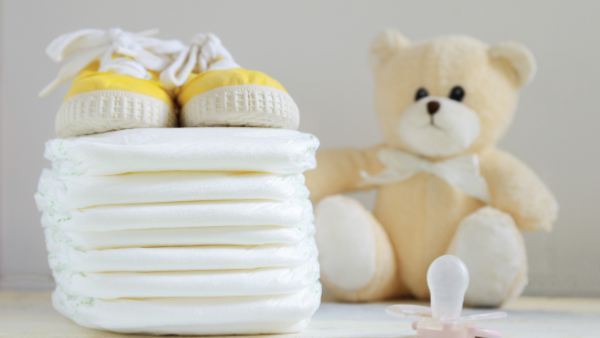 a stack of white nappies with yellow shoes on top, sitting next to a teddy bear