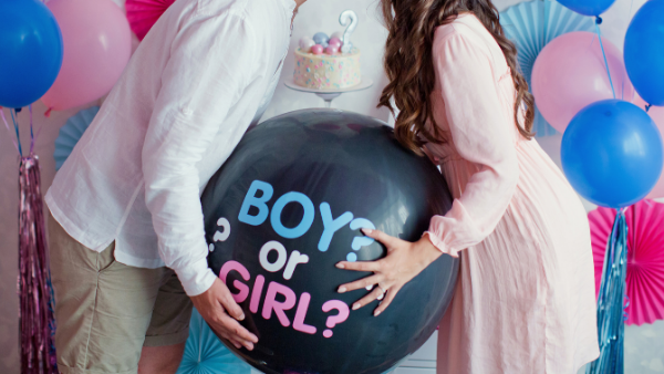 pregnant woman kissing her partner whilst holding a balloon that will reveal the baby's gender