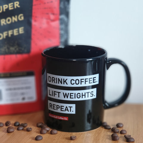 picture of black mug with drink coffee lift weights, repeat on the side, next to a bag of super strong cannonball coffee