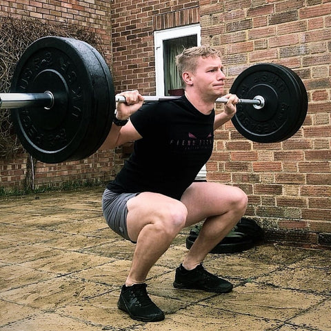 Man squatting with Olympic weights on patio 