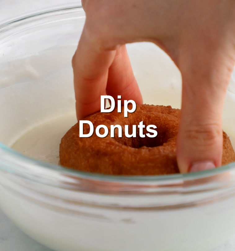 Top of plain donut being dipped into melted white chocolate