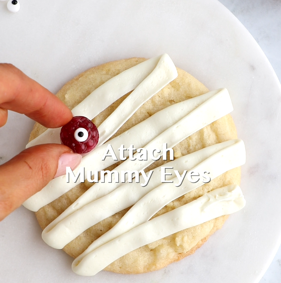 Hard candies with eyeball sprinkles being attached to Mummy Cookies