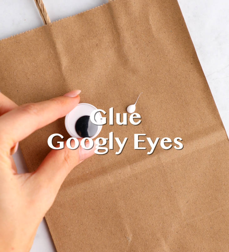 Googly eyes being glued onto a brown paper bag