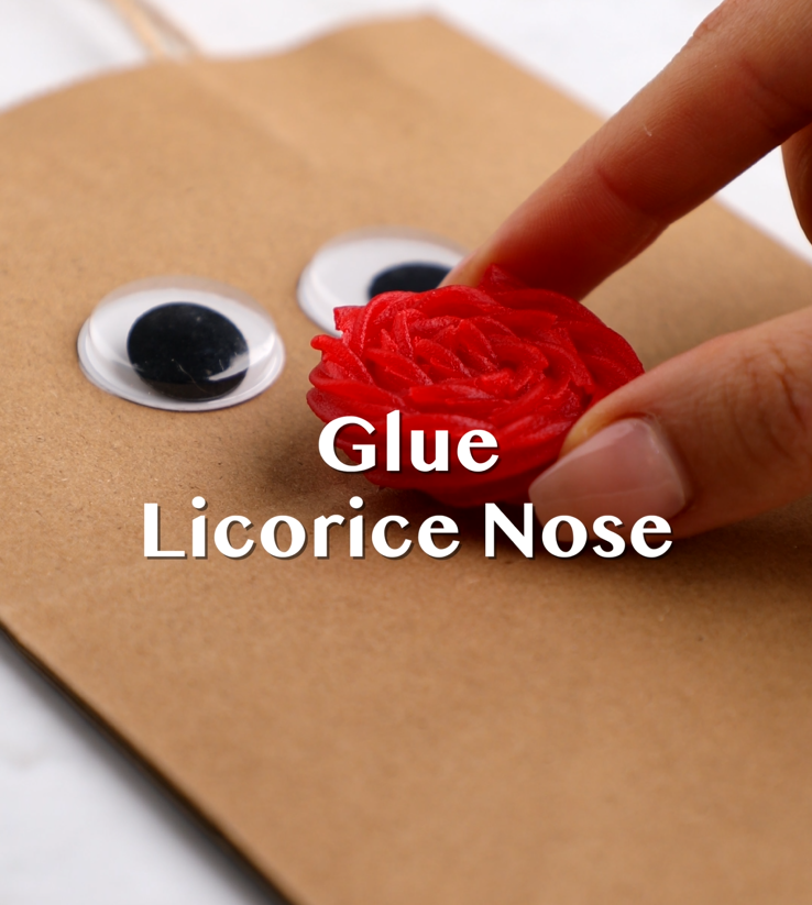 Red licorice nose being glued onto brown paper bag