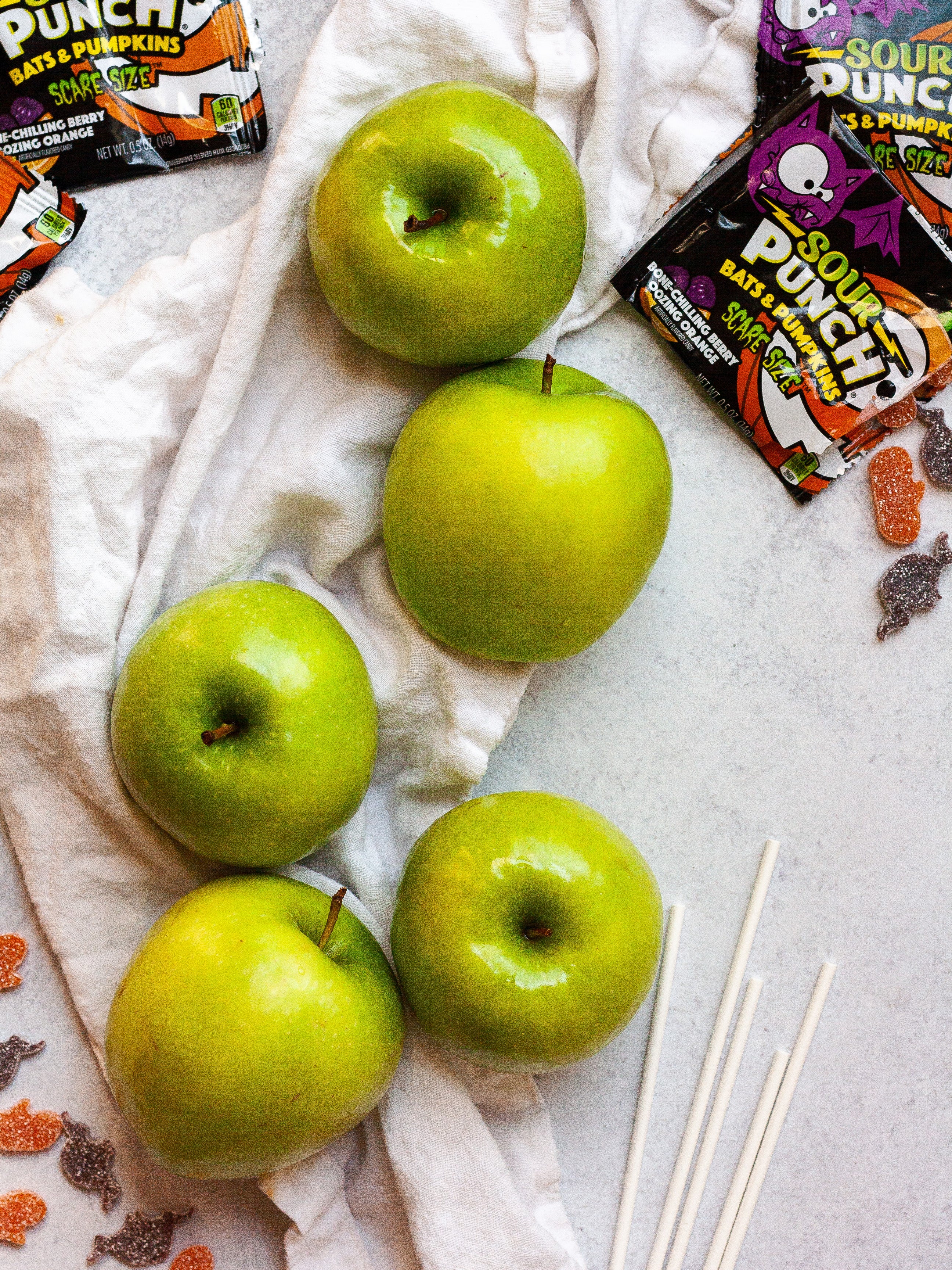 Green apples alongside lollipop sticks and Sour Punch Bats & Pumpkins candy