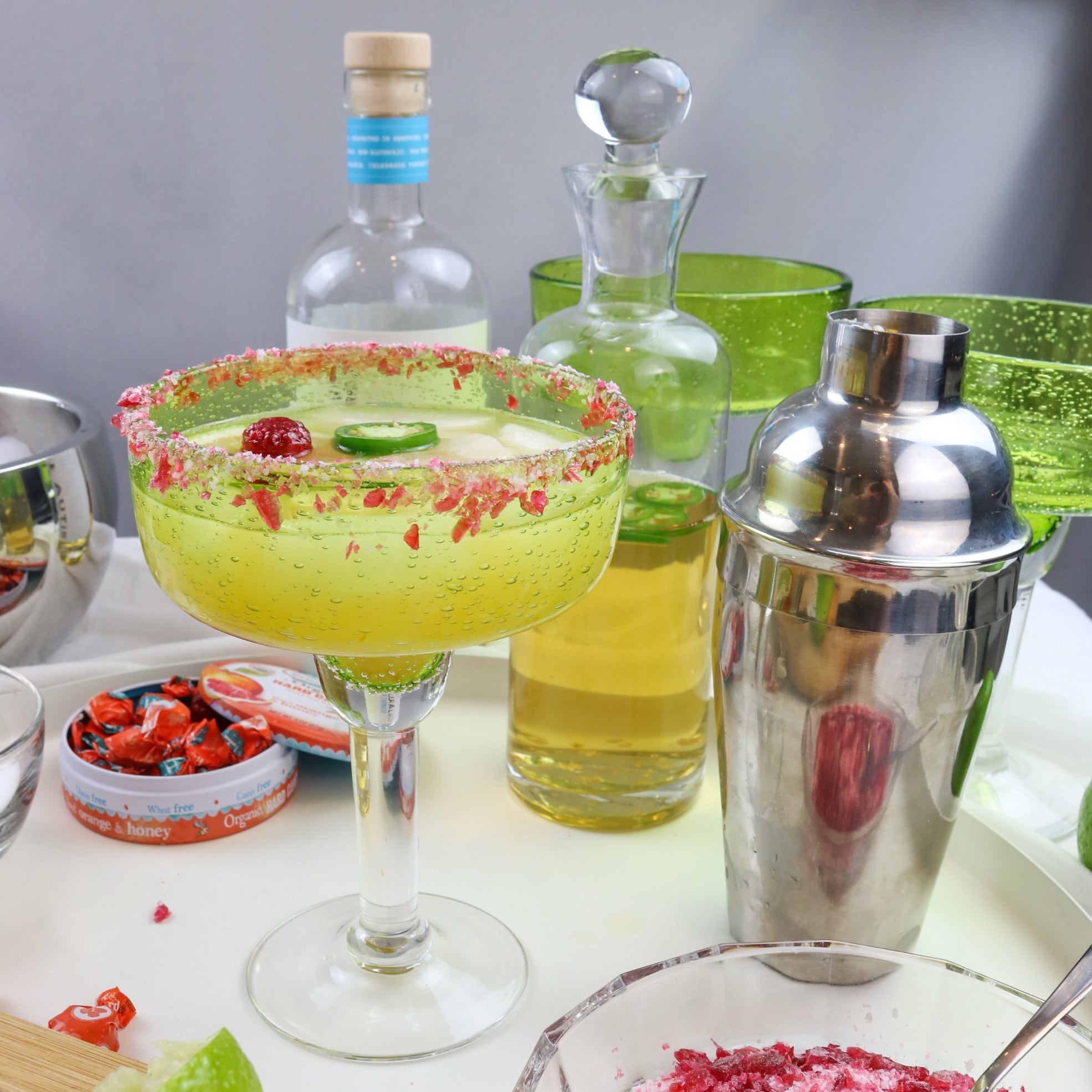 Rimmed tequila glass and mixing shaker on table with tequila and hard candies