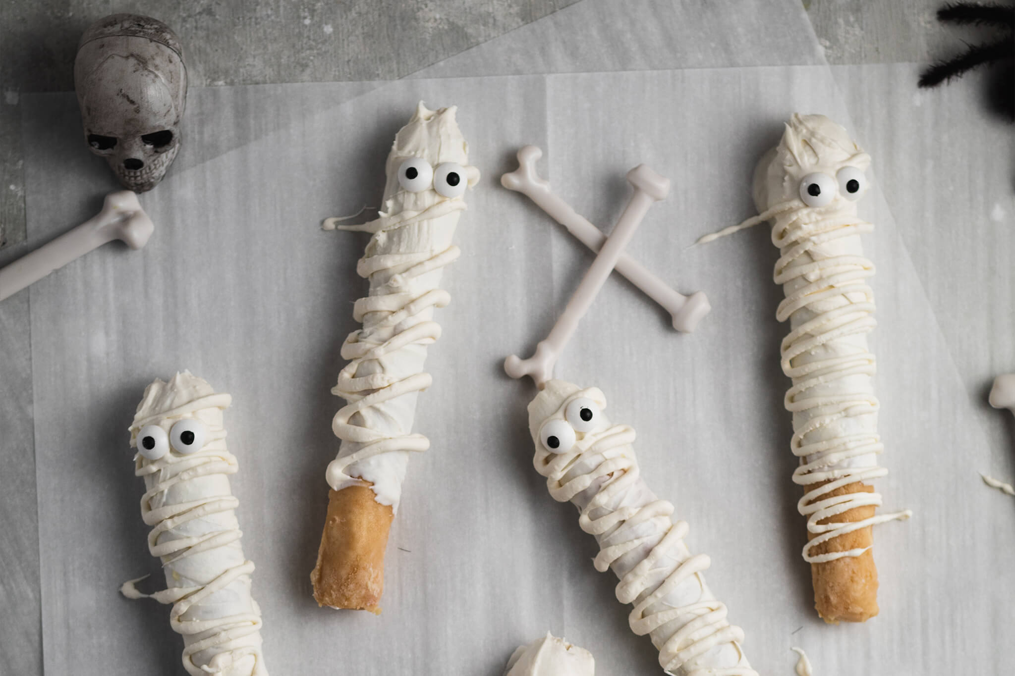 Cookie dough covered licorice dipped in white chocolate with drizzle and candy eyeballs made to look like mummies