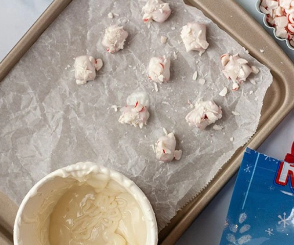 White chocolate covered licorice pieces being sprinkled with crushed peppermint candy