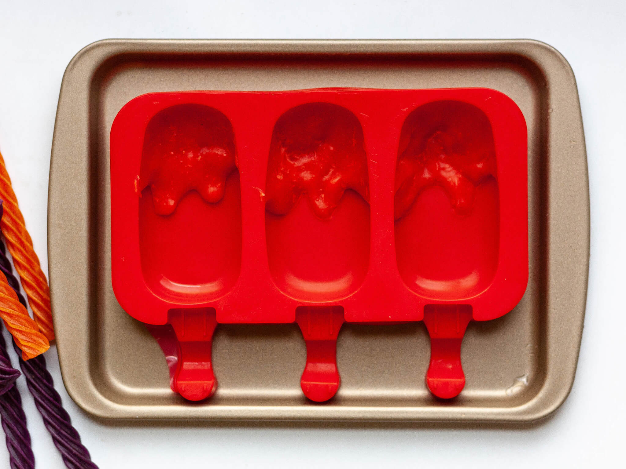 Red Vines syrup poured into the top of the popsicle trays made to look like it's dripping