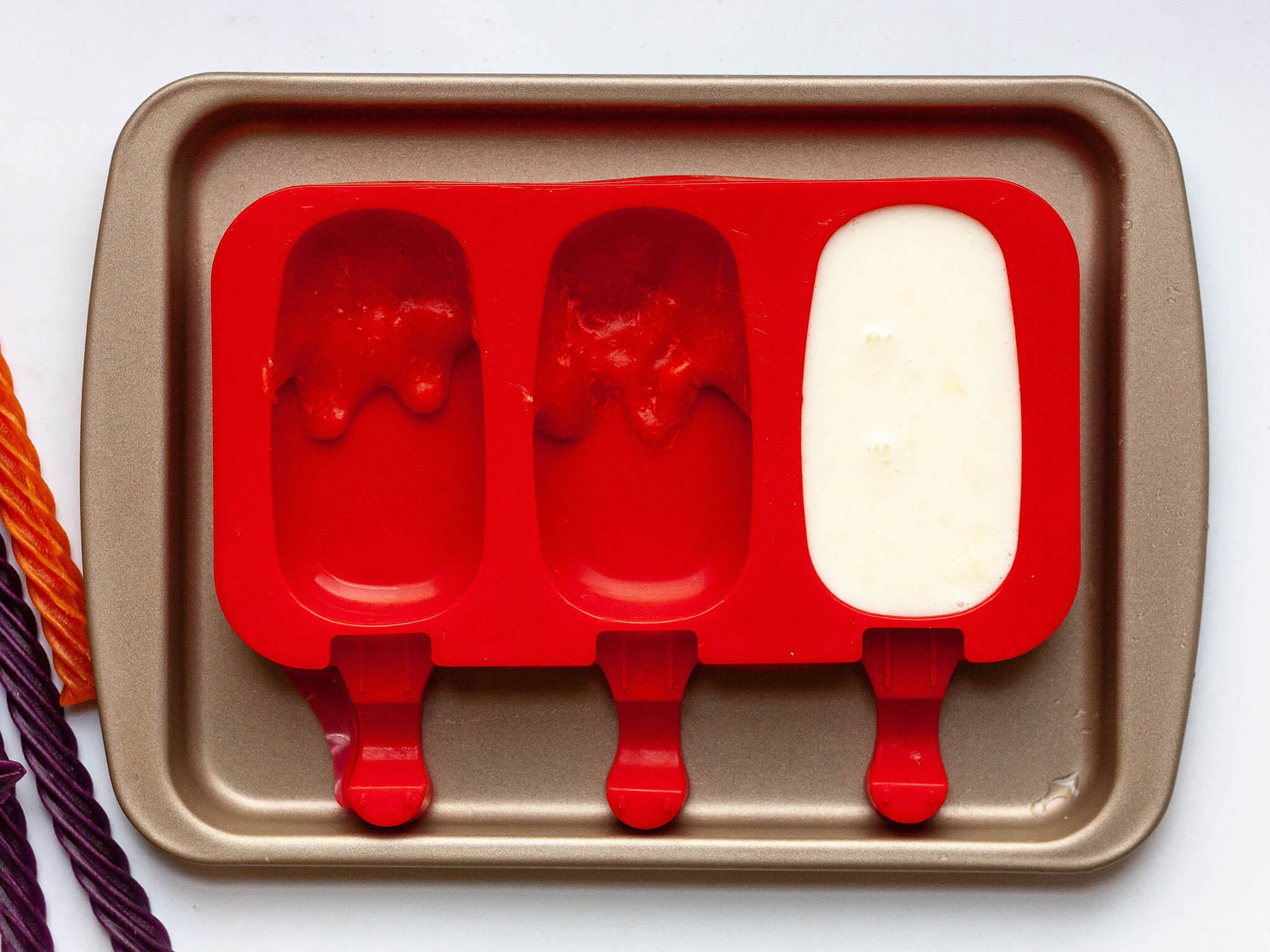 Popsicle base poured over the Red Vines syrup filling the popsicle molds