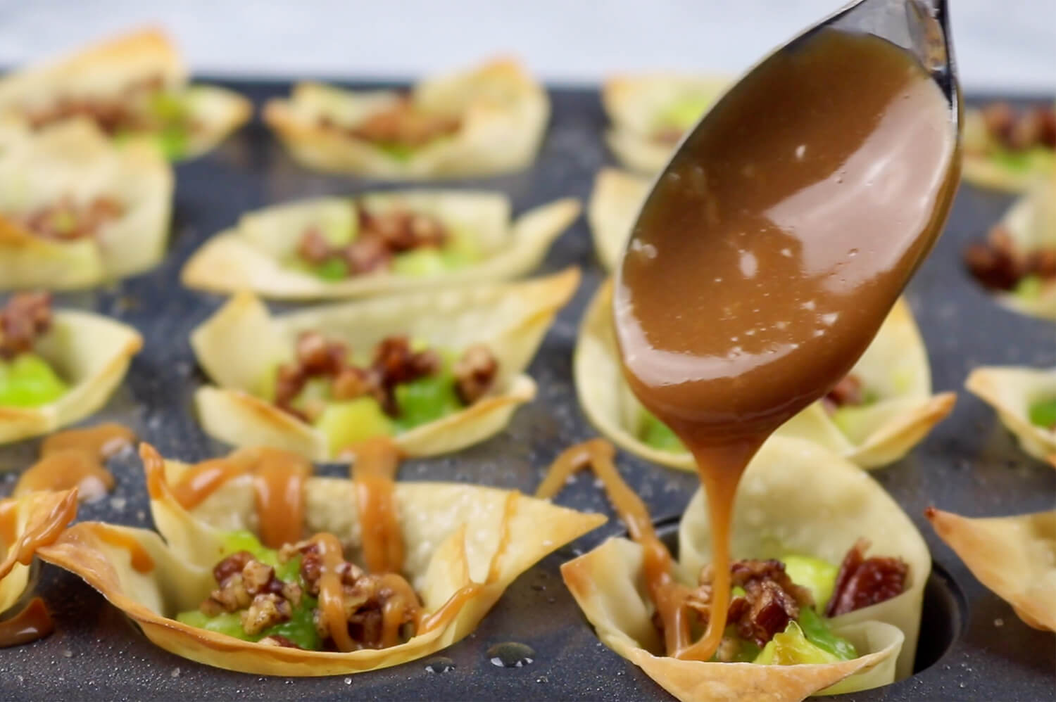 Spoon drizzling caramel over filled wonton wrappers