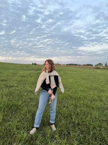 Natural fiber wool jacket for colder months in plaid tan color. Woman wearing jacket tied around shoulders in a green field of wildflowers.