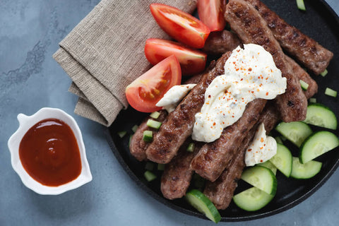 Cevapi Served With Tomatoes, Cucumber, and Kajmak
