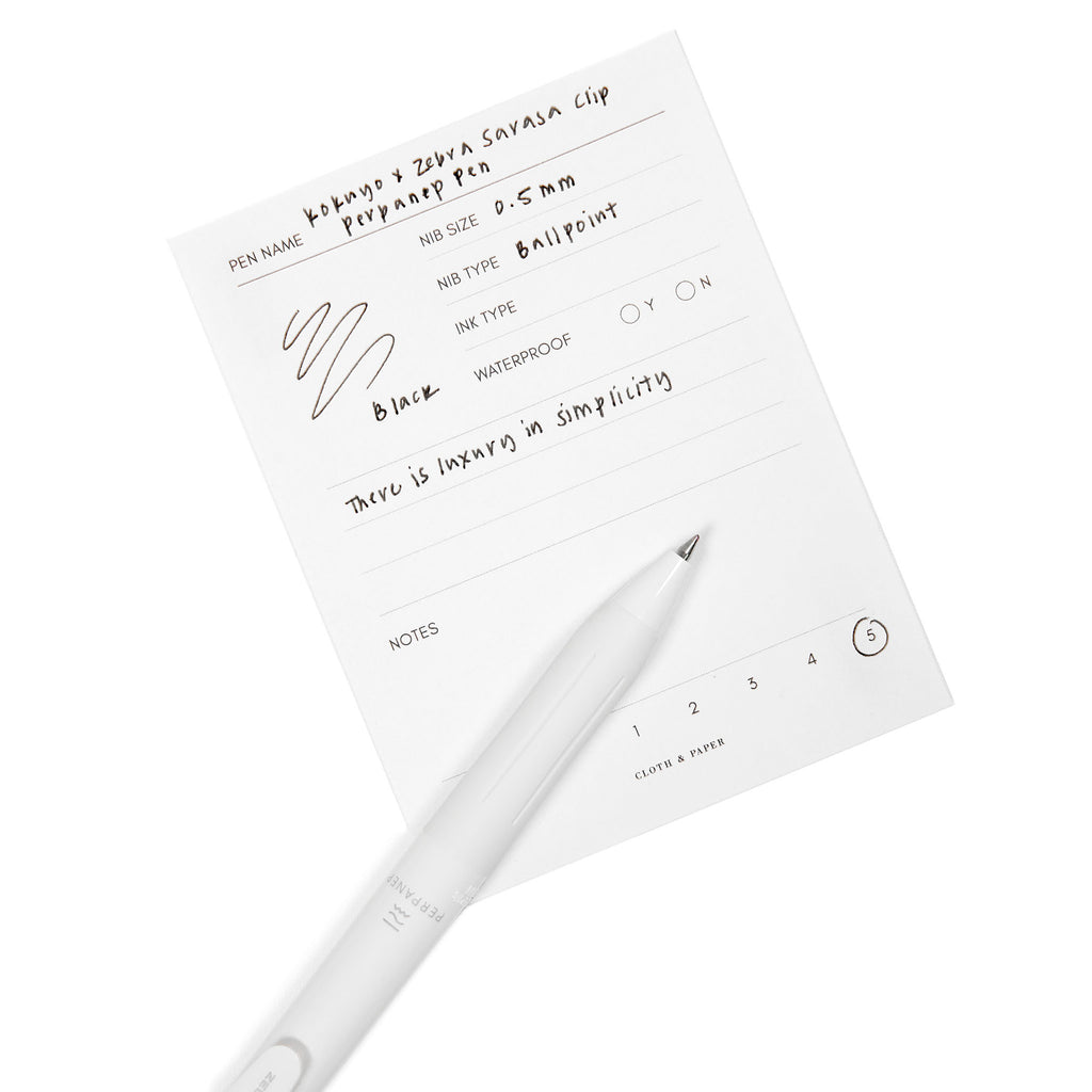 Kokuyo x Zebra Sarasa Clip Perpanep Pen, Cloth and Paper. Pen resting on pen test sheet displaying writing sample.