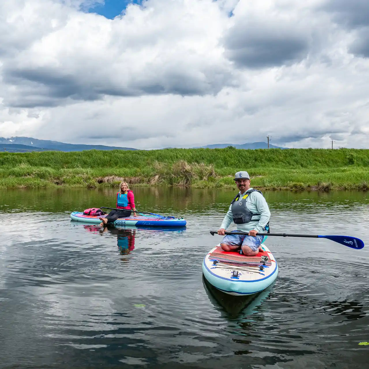 two sea gods stand up paddle boards with different art style on a river