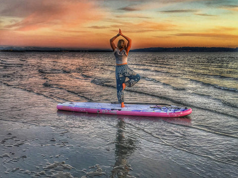 A woman in a yoga pose on the Infinite Manta board at sun rise.