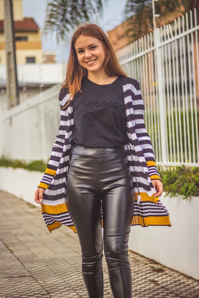 A woman wearing a cardigan with leather leggings