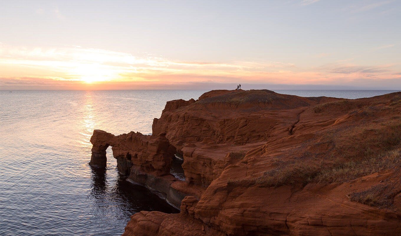 People standing with dog on immense red sandstone cliffs at Cap Hérissé, Cap-aux-Meules, Magdalen Islands, Quebec, Canada