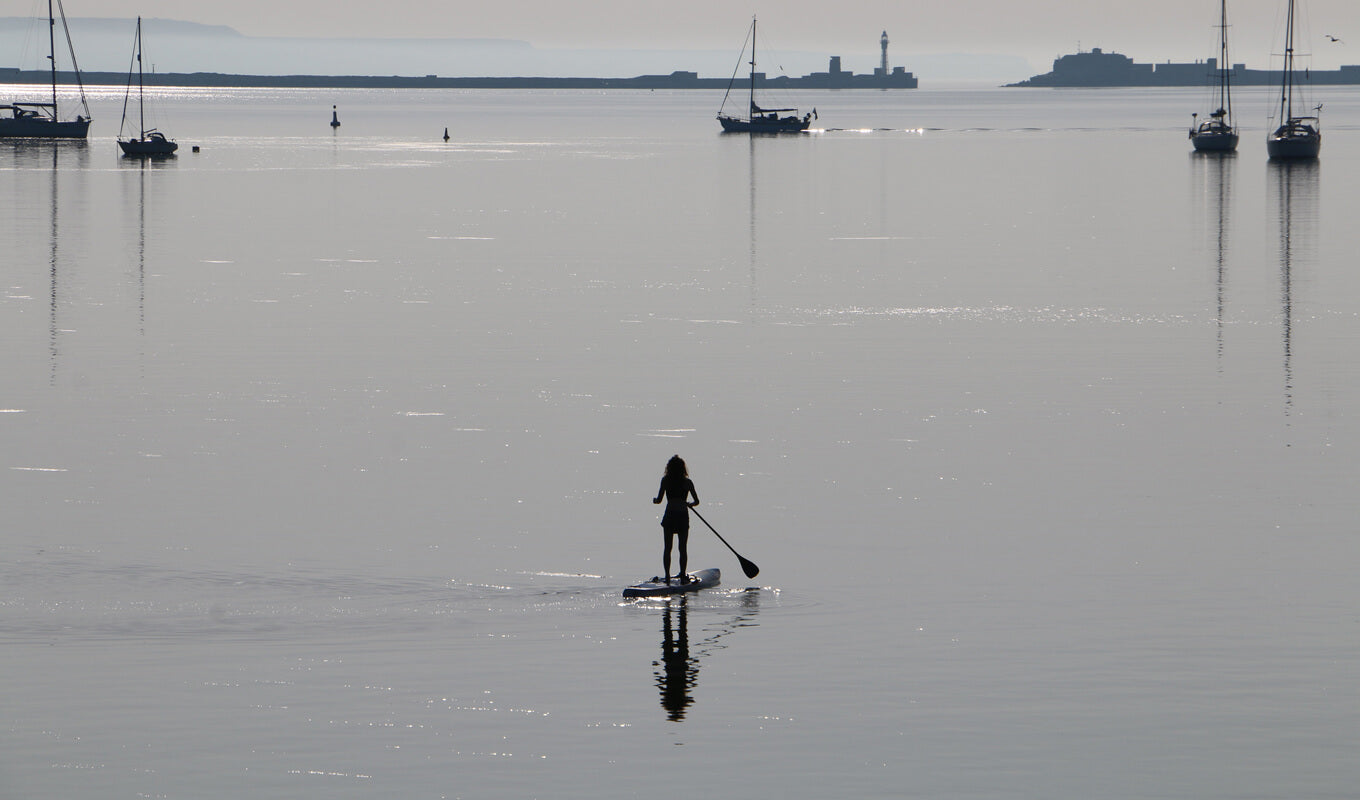 A silhouette of a woman paddle boarding at Portland Harbour