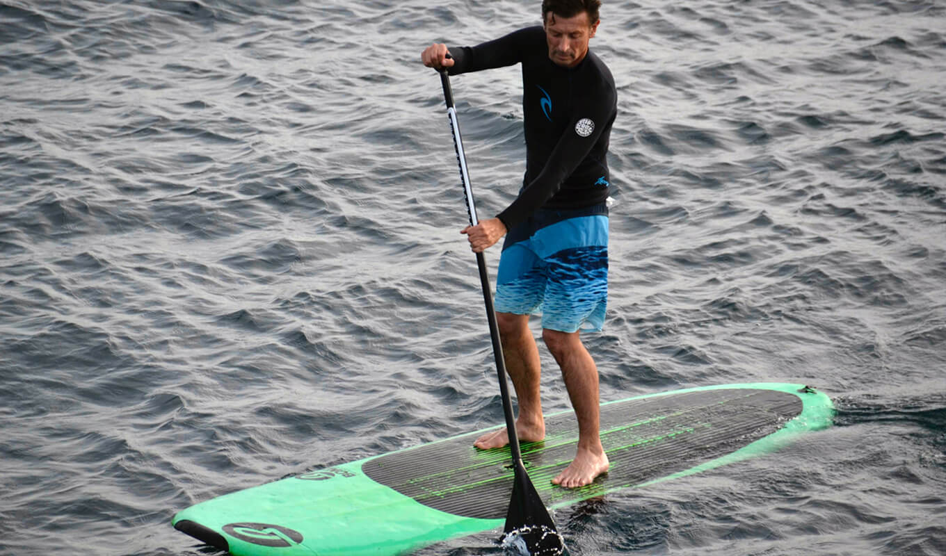 Man paddle boarding using a green soft top paddle board