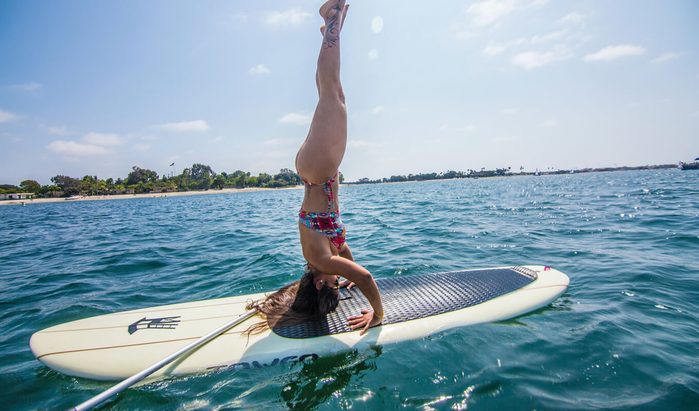 Woman performing yoga on a soft top paddle board