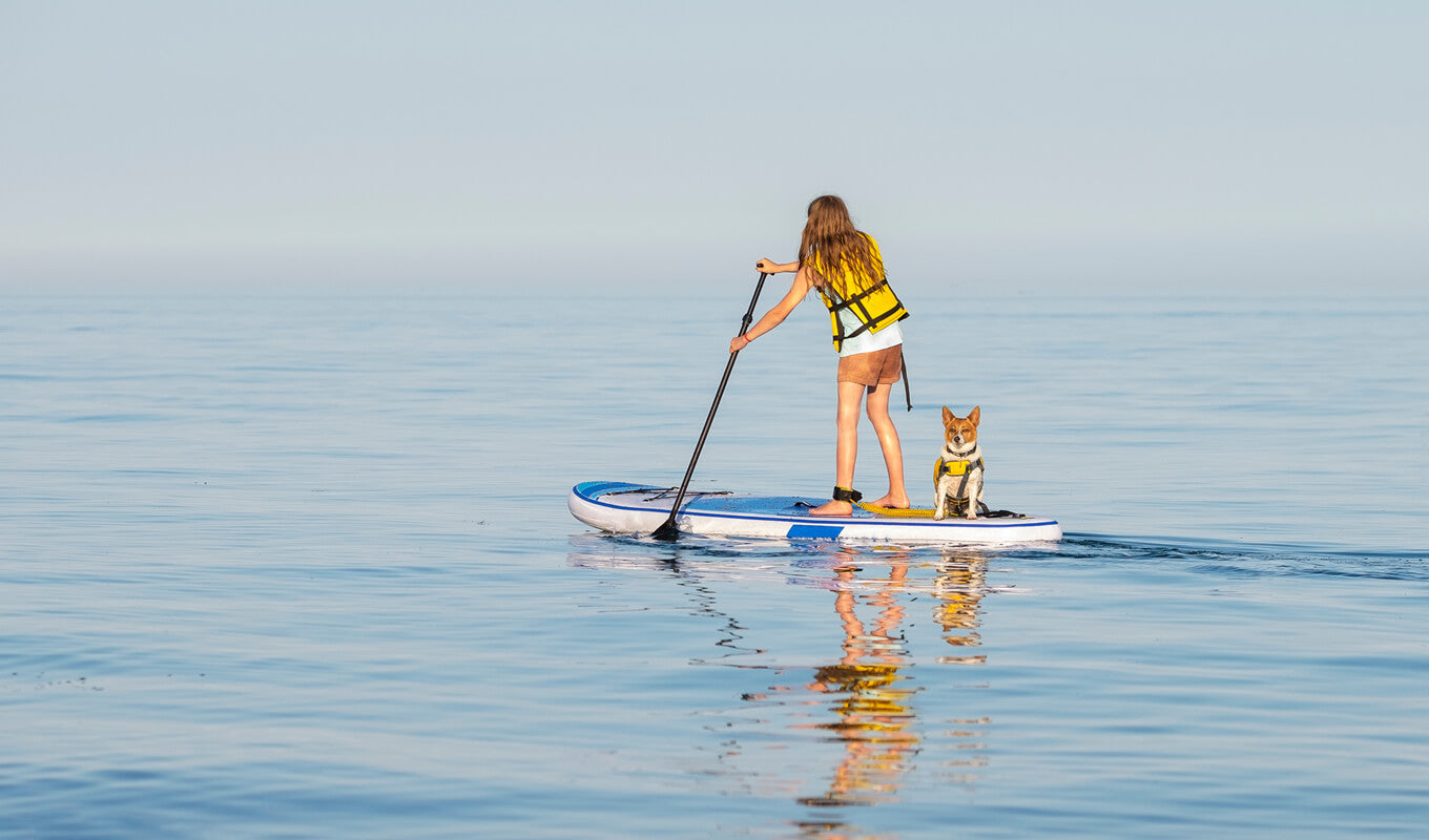 Kid wearing a life jacket paddle boarding with her dog