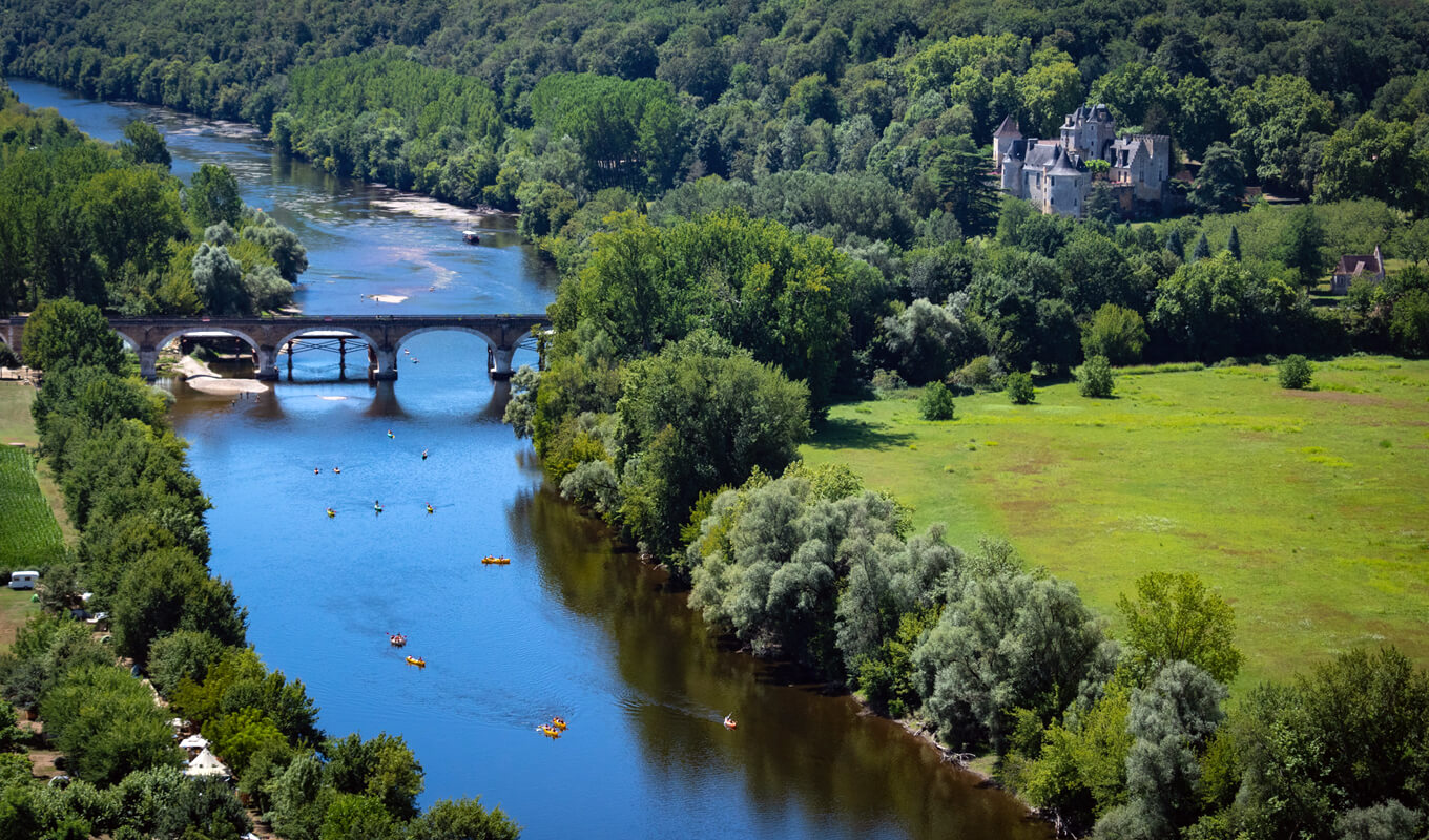 Kayakers on Dordogne river near a medieval bridge